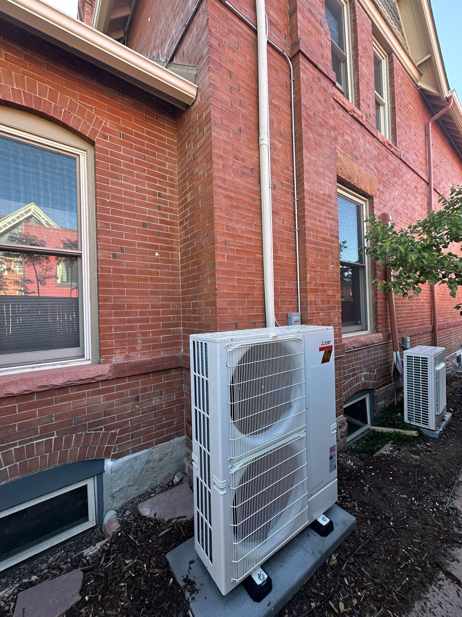 Mitsubishi Hyper-Heat outdoor unit beside a Victorian brick home in Denver