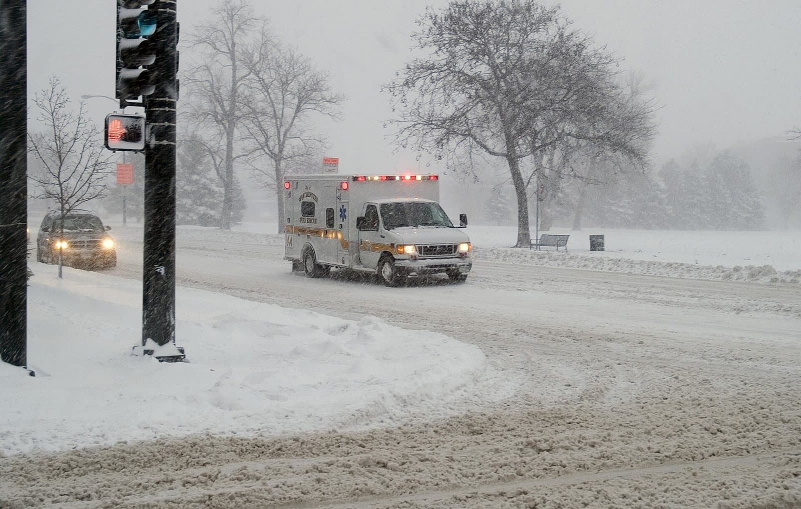 An ambulance driving through deep snow on a Denver metro street during a blizzard