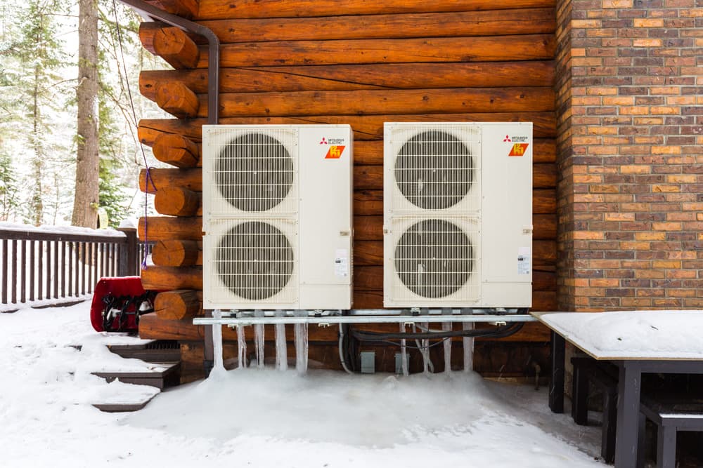 Two Mitsubishi Hyper-Heat outdoor units running in snow beside a Colorado log home