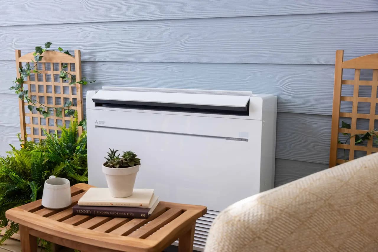 Mitsubishi floor-console mini-split indoor unit on a patio with light blue siding