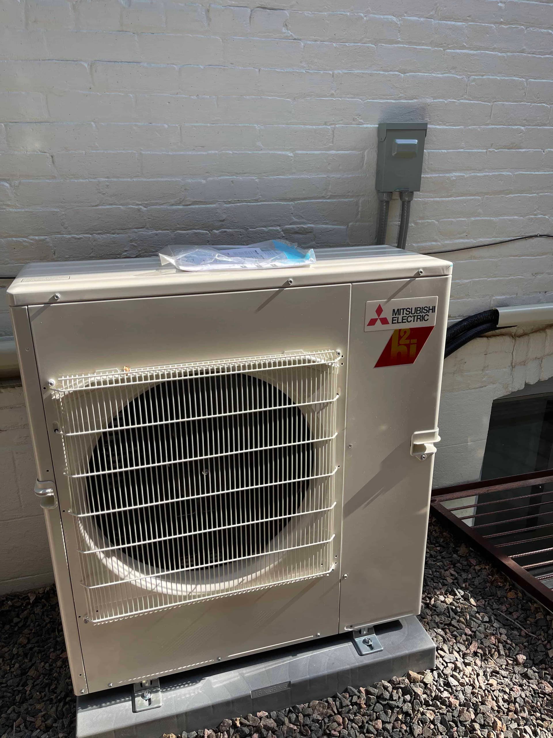 Mitsubishi heat pump outdoor unit on concrete pad beside brick wall