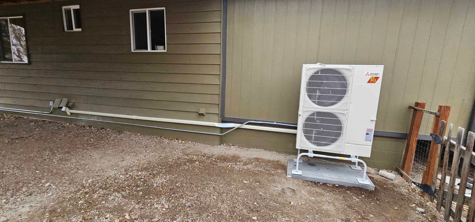 Small single-zone Mitsubishi mini split outdoor unit on a concrete pad by a wooden fence