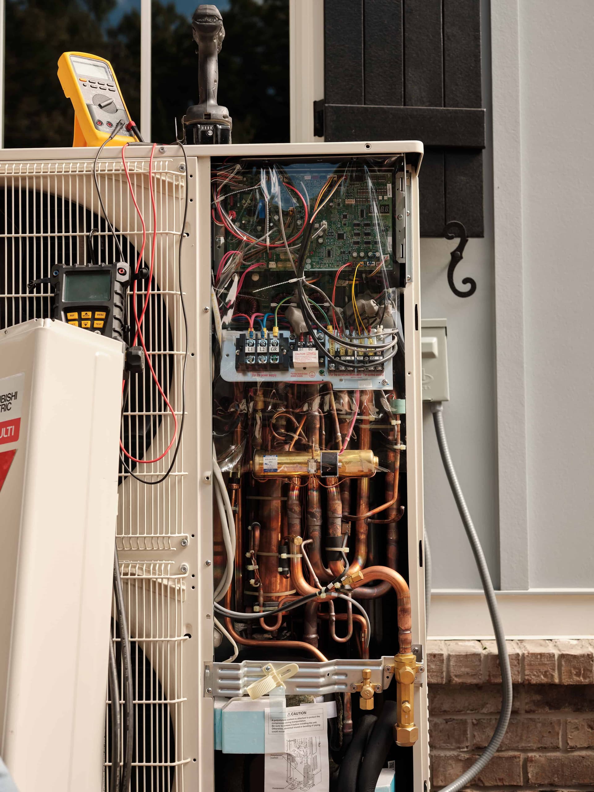 Mitsubishi outdoor condenser unit being serviced with multimeter