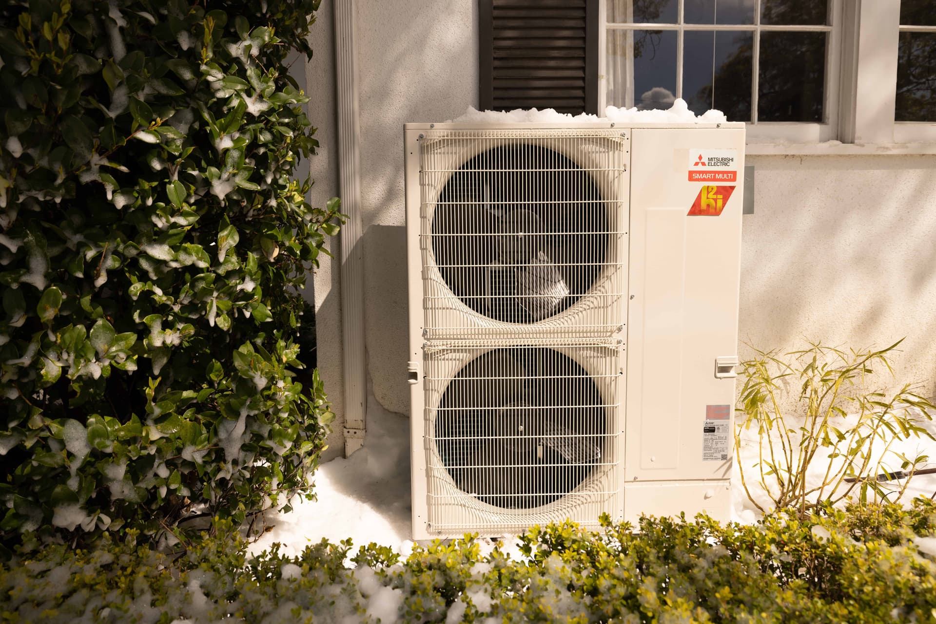 Mitsubishi Smart Multi H2i condenser with snow on top outside a white Denver home