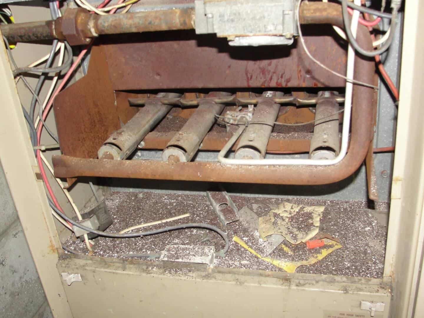 Heavily rusted gas furnace burner assembly with four deteriorated tubes exposed inside furnace cabinet