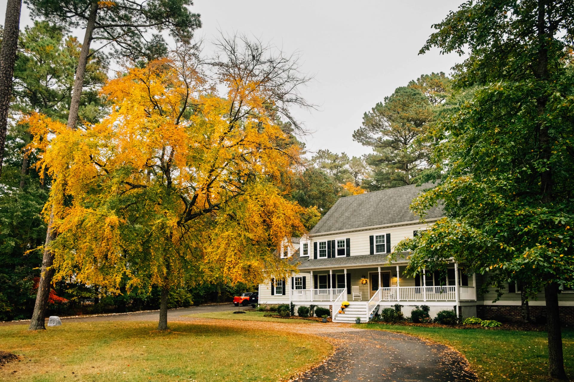 White two-story house with black shutters and autumn trees