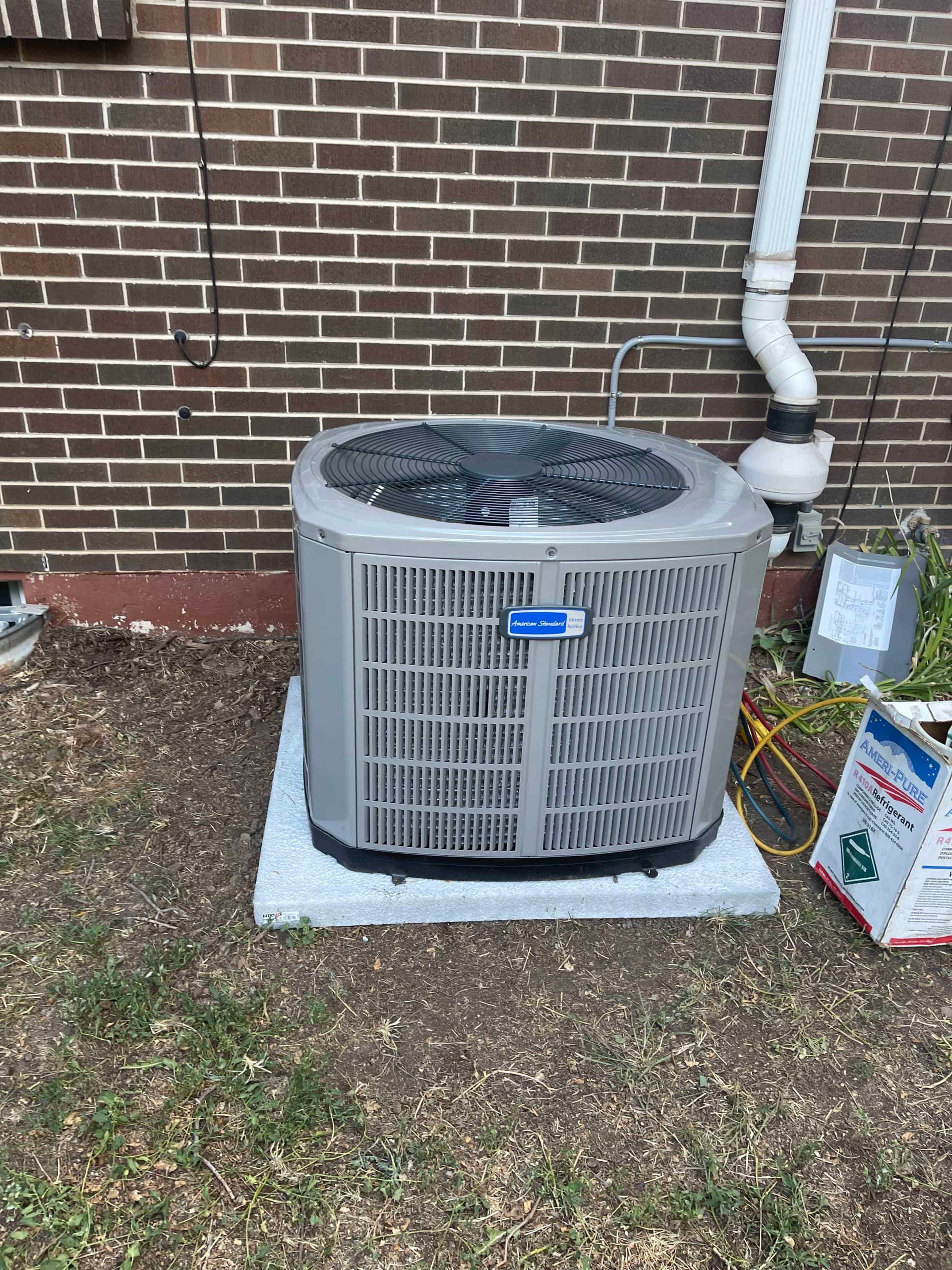 American Standard outdoor condenser unit on concrete pad against brick wall