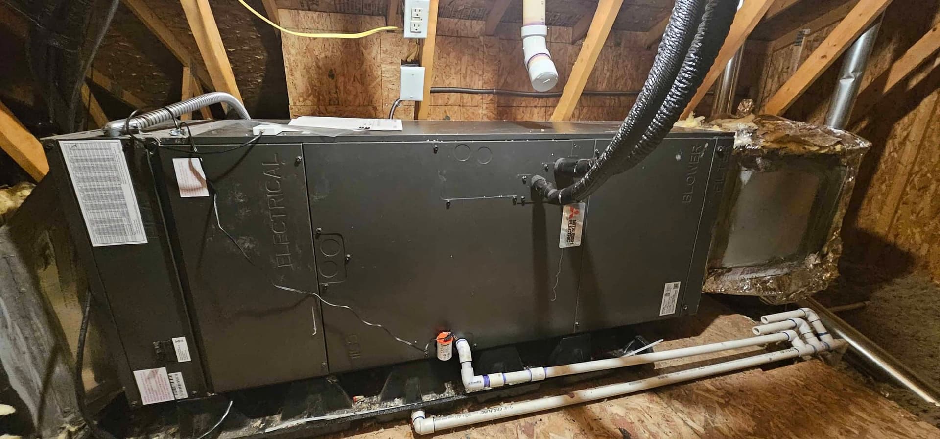 HVAC installation in attic with exposed beams and electrical label