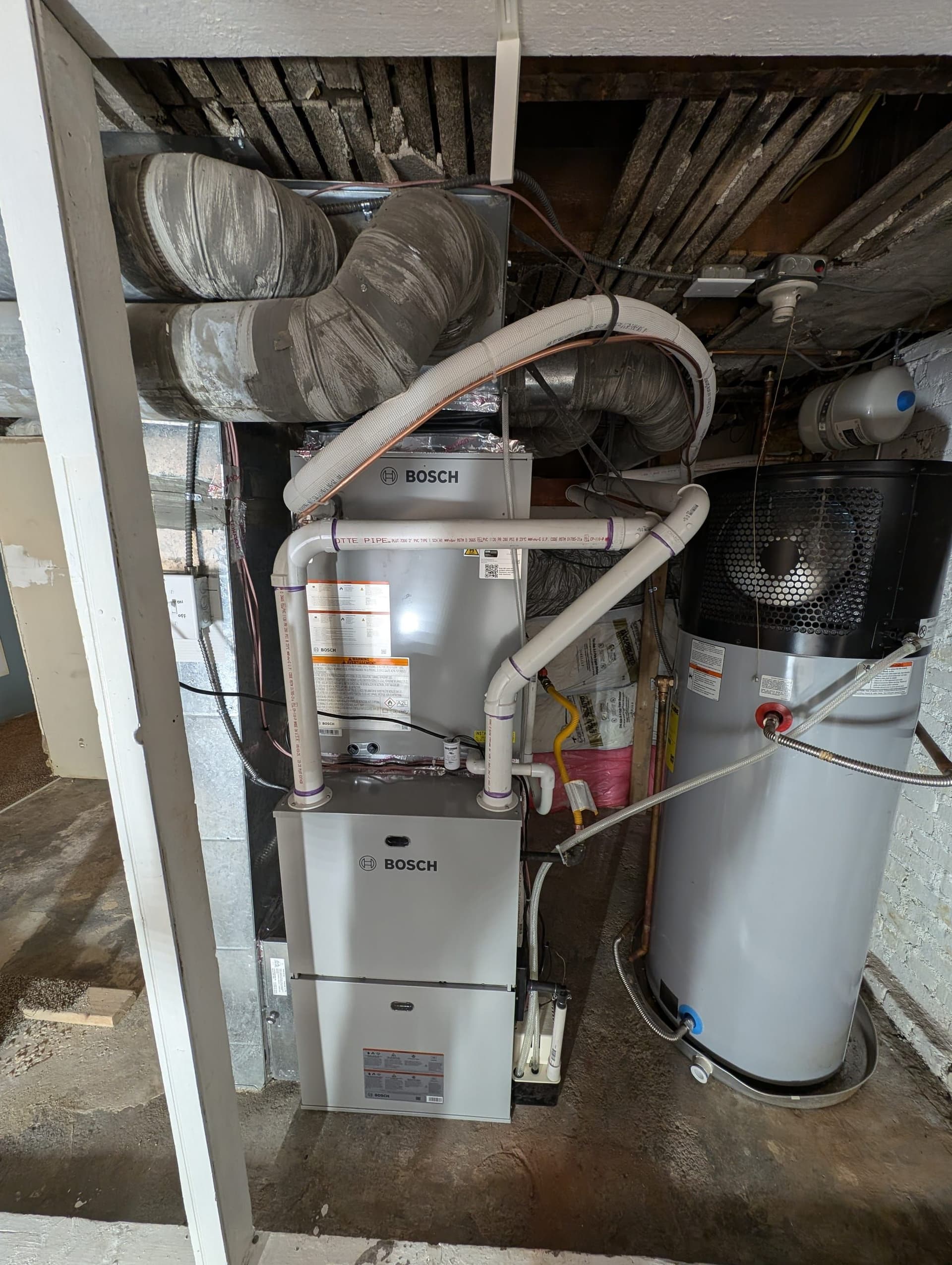 Bosch furnace, air handler, and water heater in basement with pink bucket