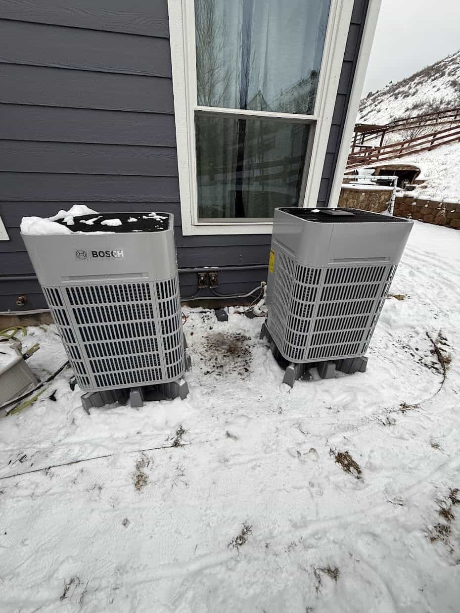 Two Bosch heat pump outdoor units installed outside a Colorado home with snow on the ground and mountains in the background