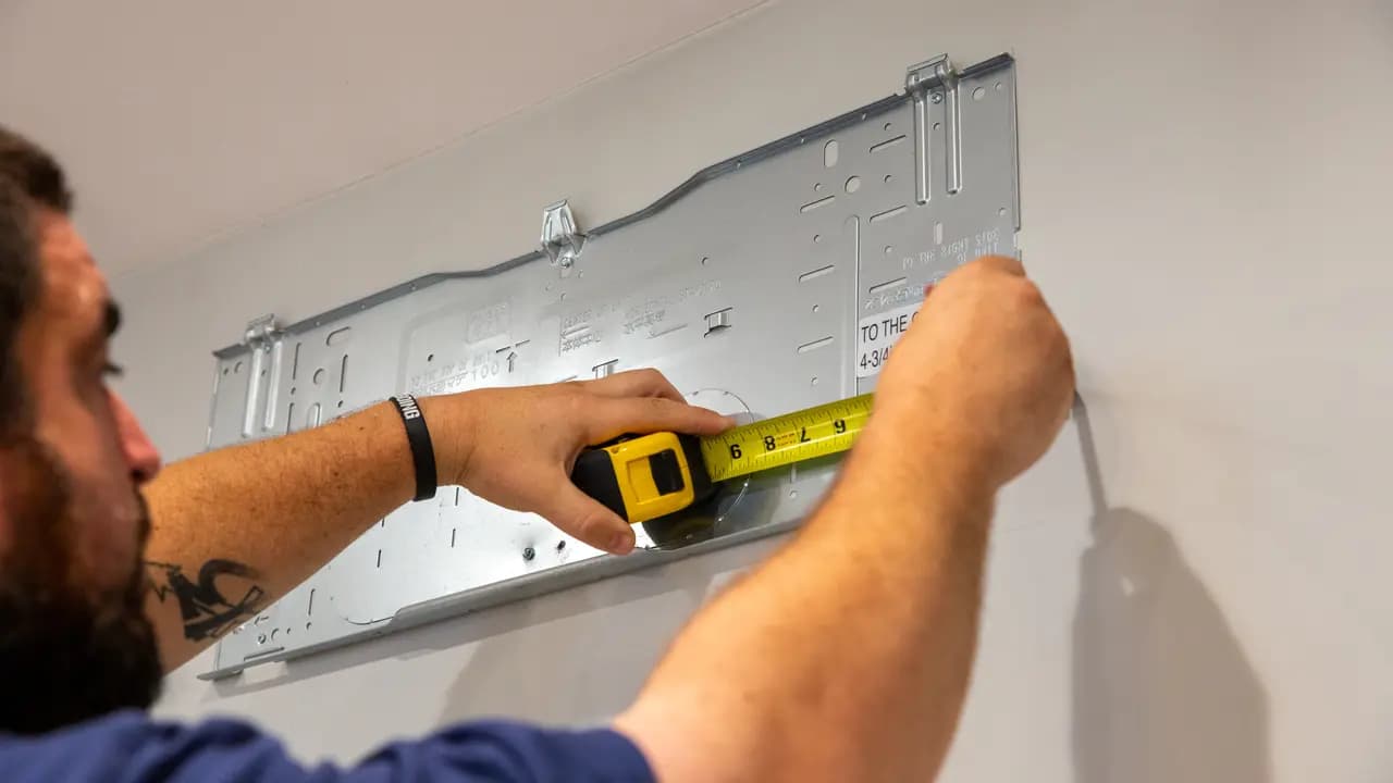 Technician measuring and mounting a mini-split wall bracket during installation