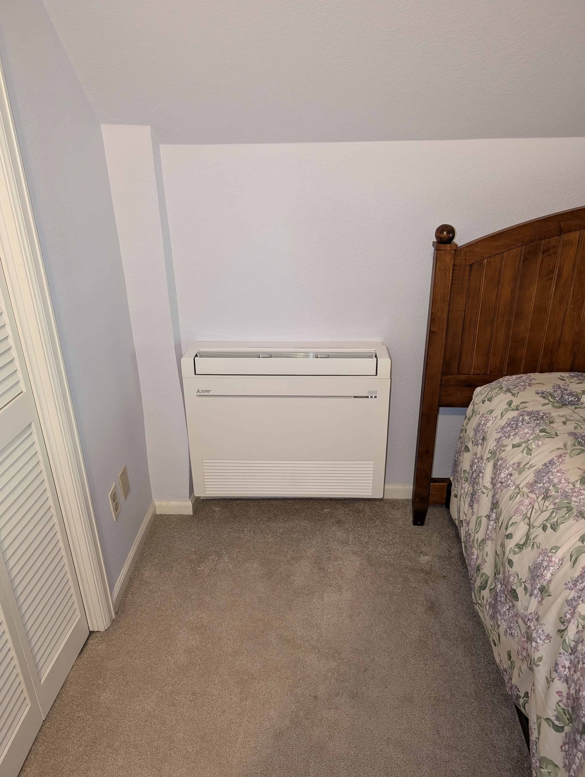 Mitsubishi mini-split indoor unit on light blue wall above a wooden bed
