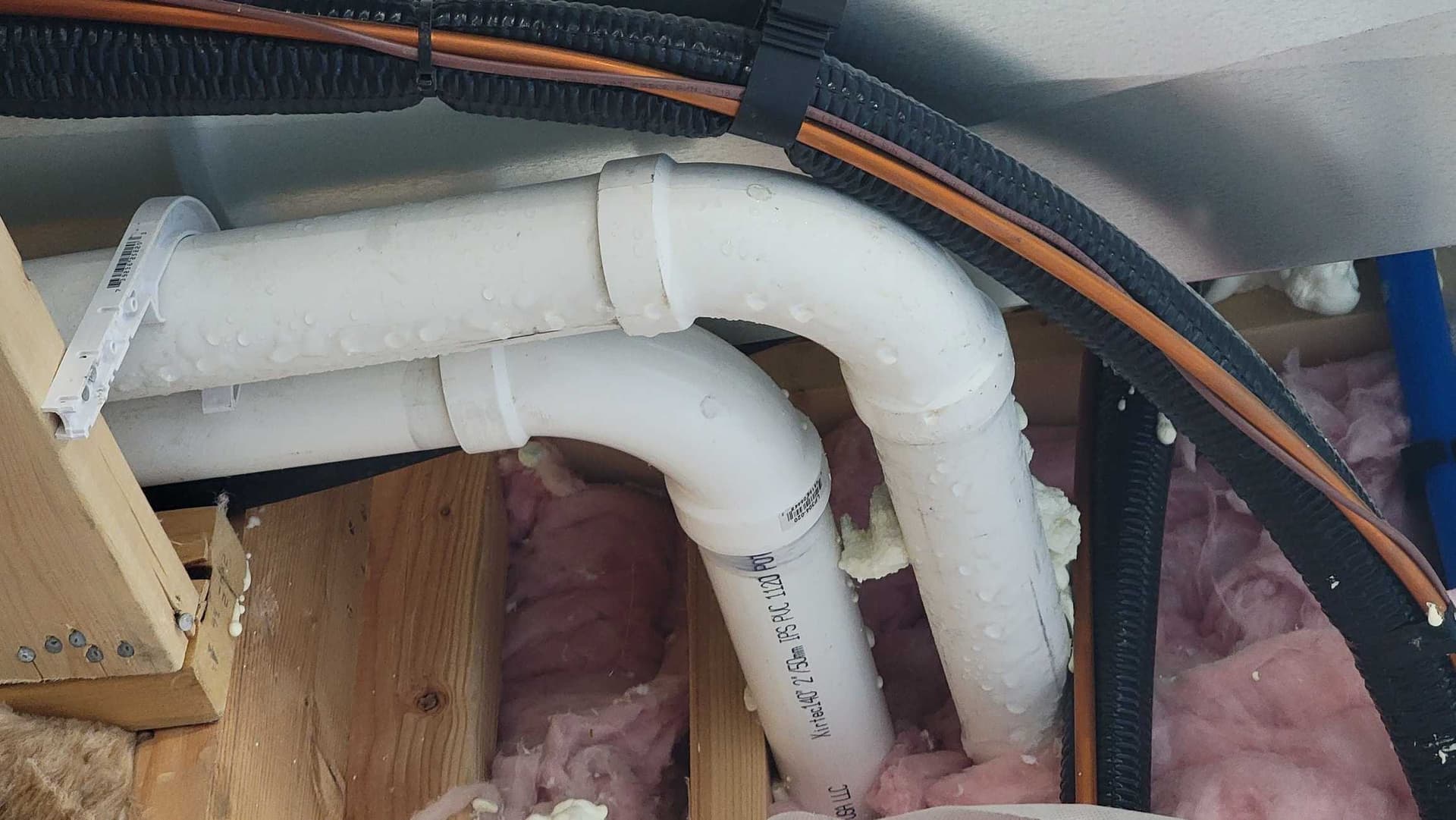 PVC pipes in attic with pink insulation visible