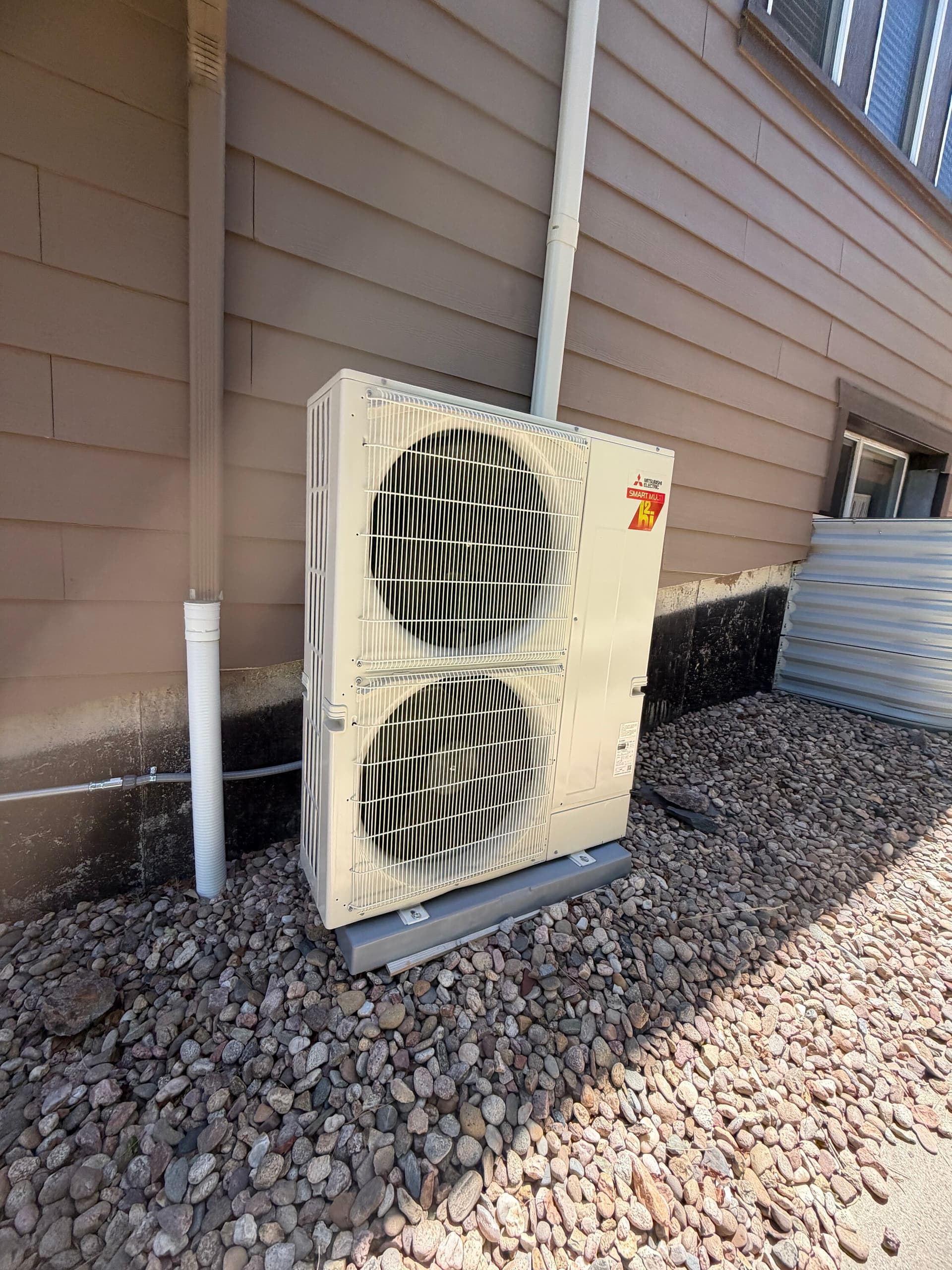 Mitsubishi hyper-heat outdoor unit installed on a stand beside a Denver home