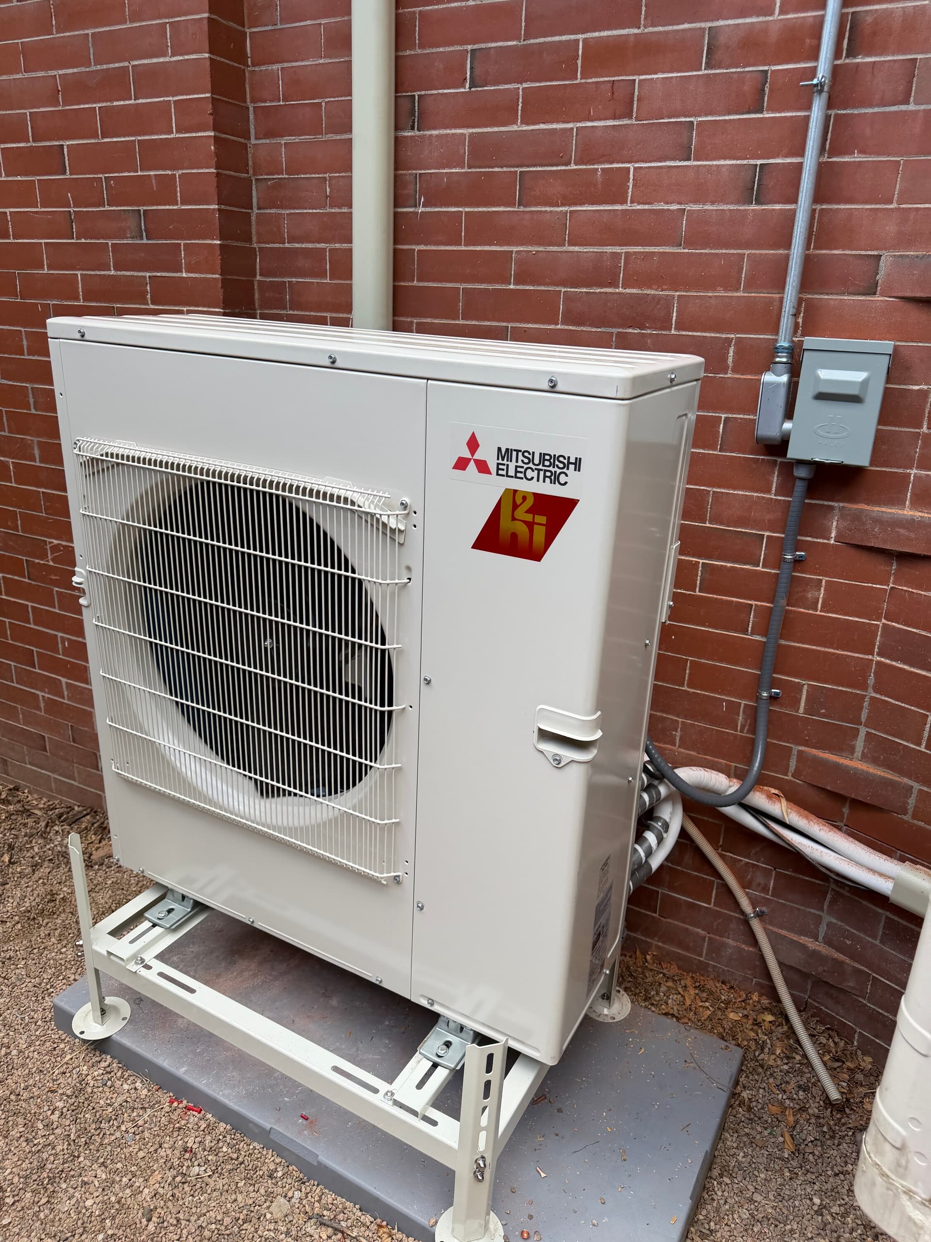 Mitsubishi Hyper-Heat outdoor unit on a stand beside a brick Denver home