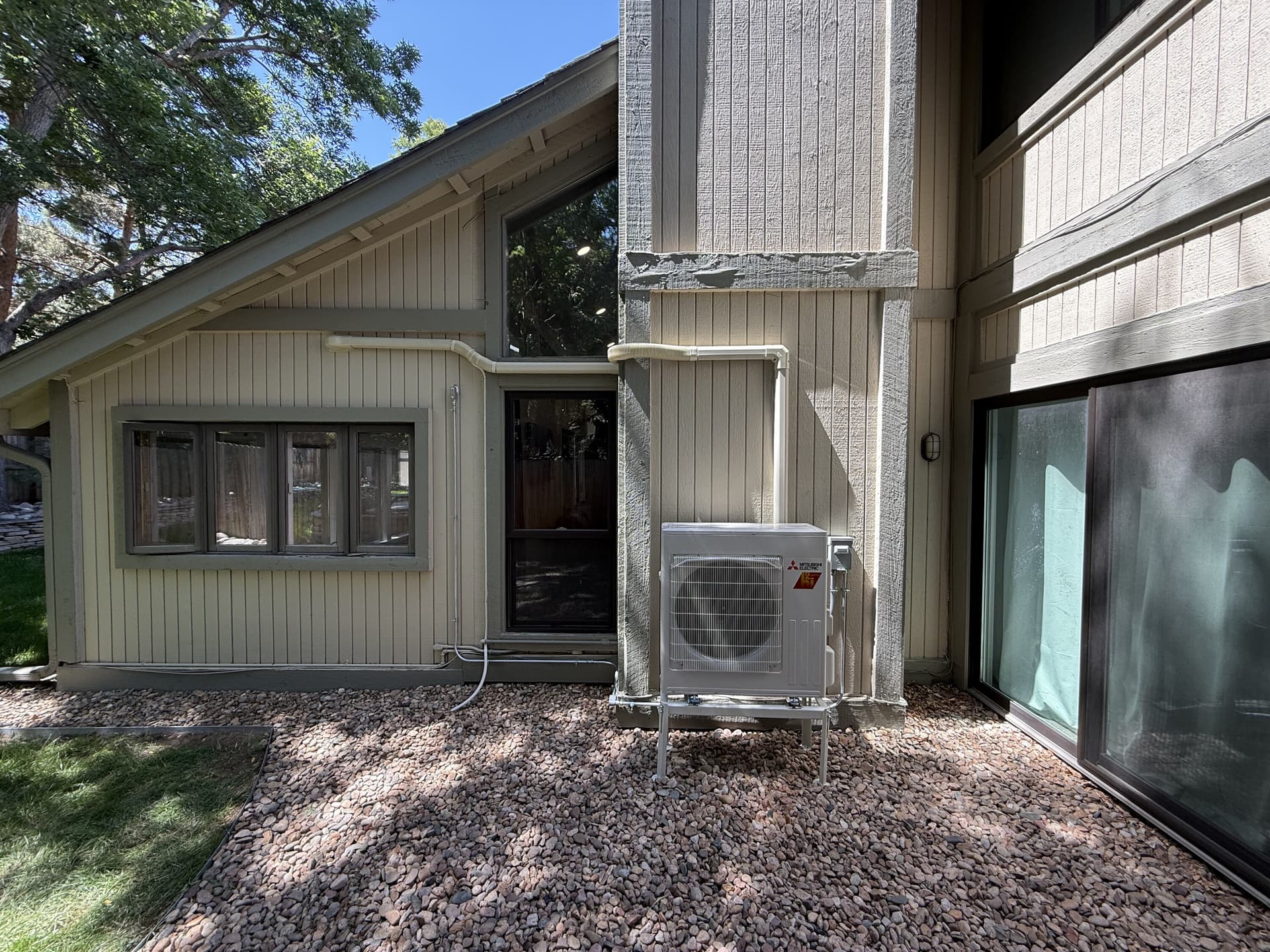 Mitsubishi heat pump outdoor unit on a stand with covered line sets beside a Denver-area home